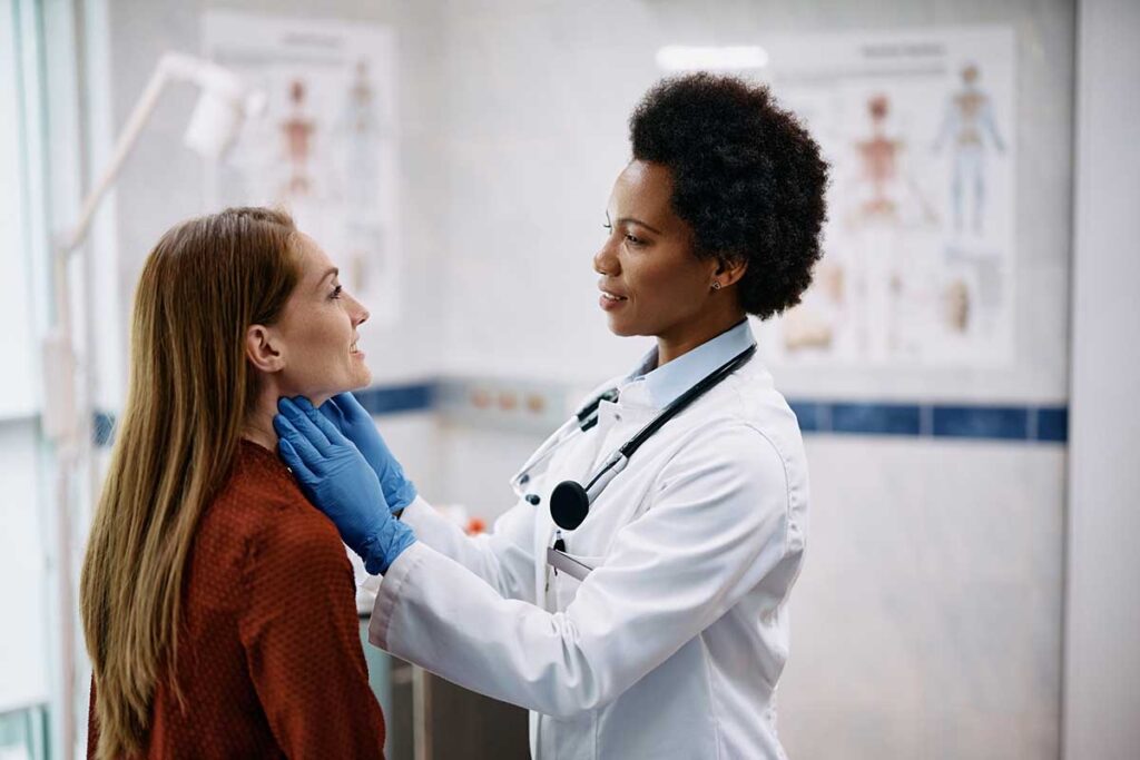 A physician examines her patient's thyroid in an exam room.