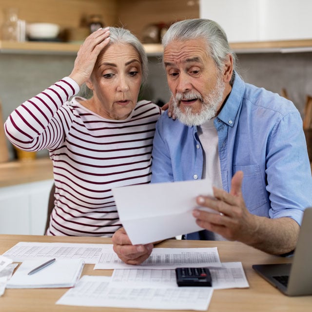 A couple sitting at a table looking at papers in shock