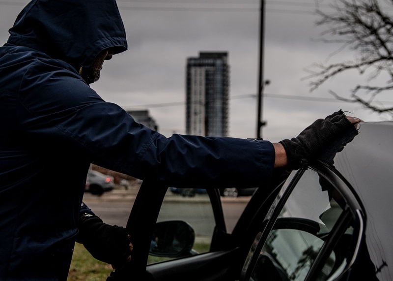 A thief breaking into a car in broad daylight in Toronto.